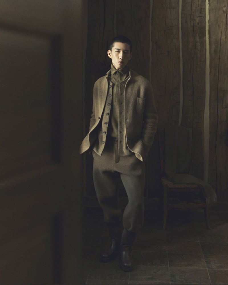 Long Li wears an olive jacket over layered knitwear with dark trousers inside a wooden chalet.