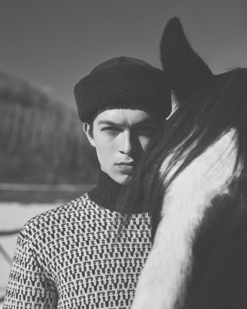 Just Verhoeff wears a patterned sweater and knit cap beside a horse in a black-and-white portrait.