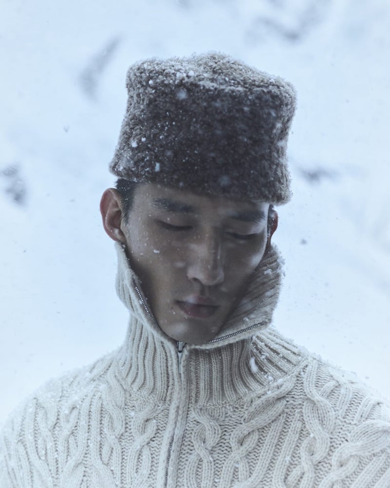 Long Li wears a cream cable-knit turtleneck and textured hat dusted with snow.