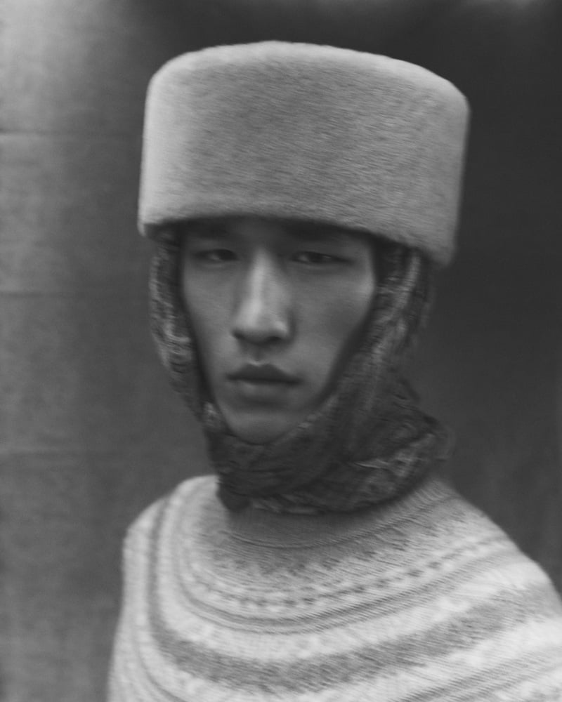 Long Li wears a patterned sweater, scarf, and light-colored hat in a black-and-white portrait.