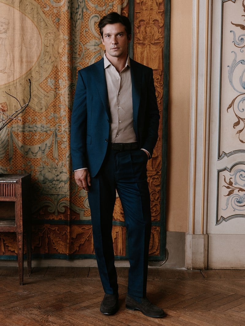 A man wears a dark blue suit with a black shirt.