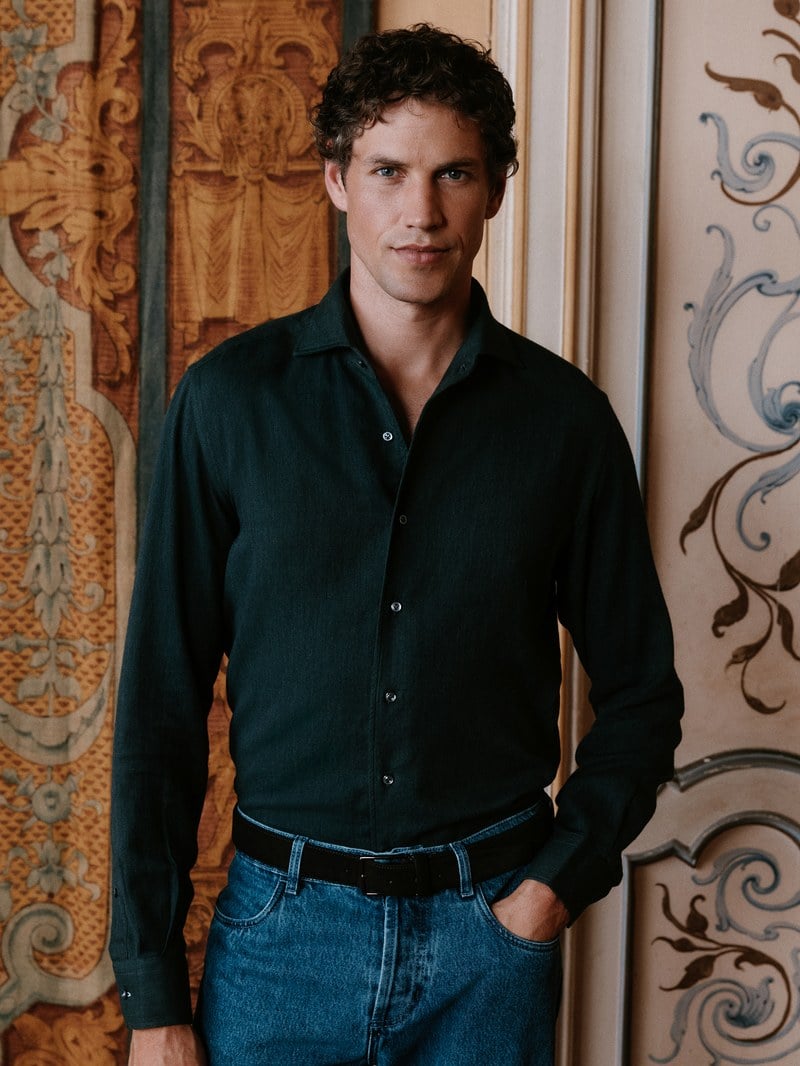 A man wears a dark open-collar shirt with blue jeans.