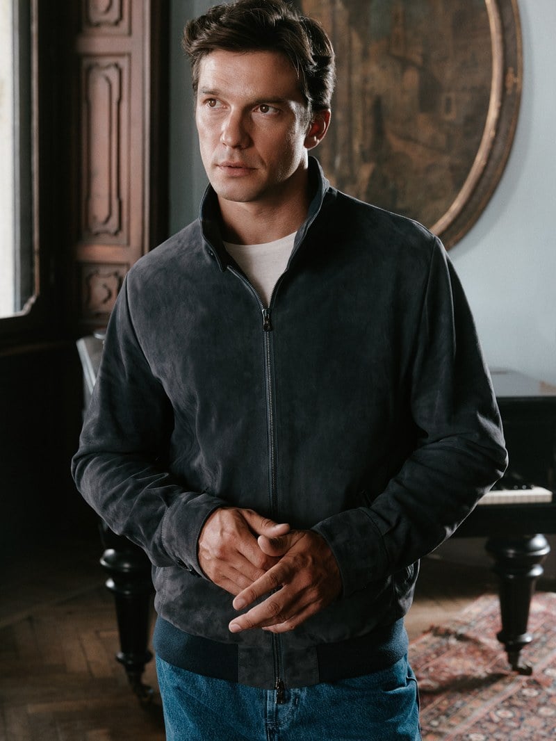 A man wears a charcoal zip cardigan over a white T-shirt with blue jeans.