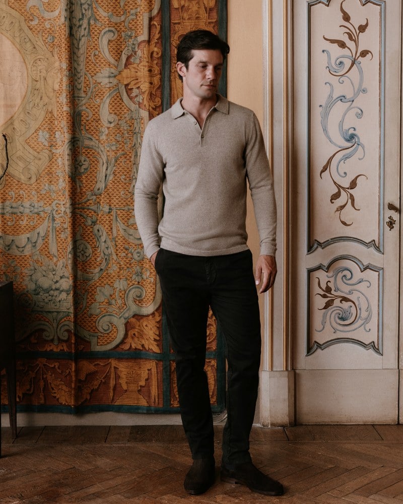 A man wears a beige knit quarter-zip with dark trousers.