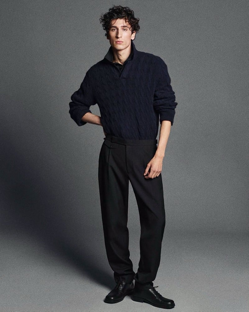 Lucien Le Neve wears a dark cable-knit cashmere sweater with pleated trousers and black shoes.