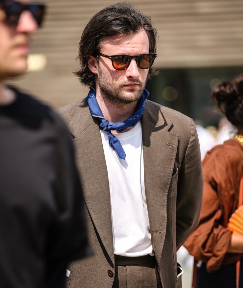 Man in a brown textured suit, white tee, blue bandana and tinted sunglasses