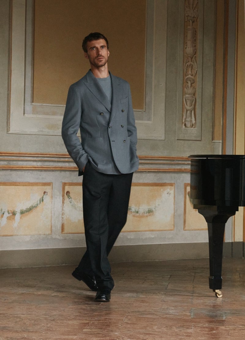 Clément Chabernaud wears a double-breasted blazer over knitwear with trousers beside a piano.
