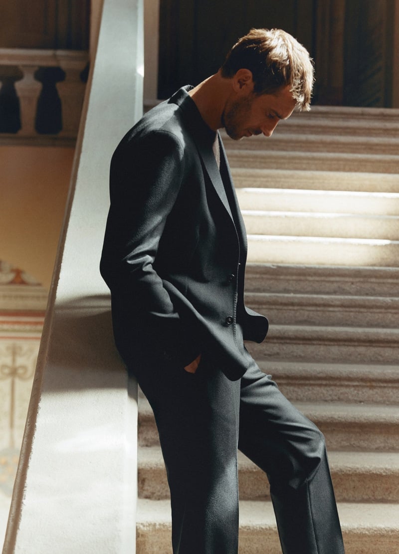 Clément Chabernaud walks beside a staircase in a dark blazer and tailored trousers.