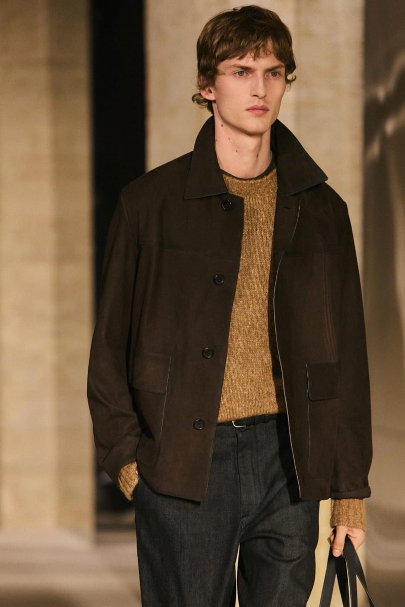 Massimo Dutti Limited Edition fall-winter 2026: Model wears a dark brown jacket over a textured ochre sweater with charcoal pleated trousers.