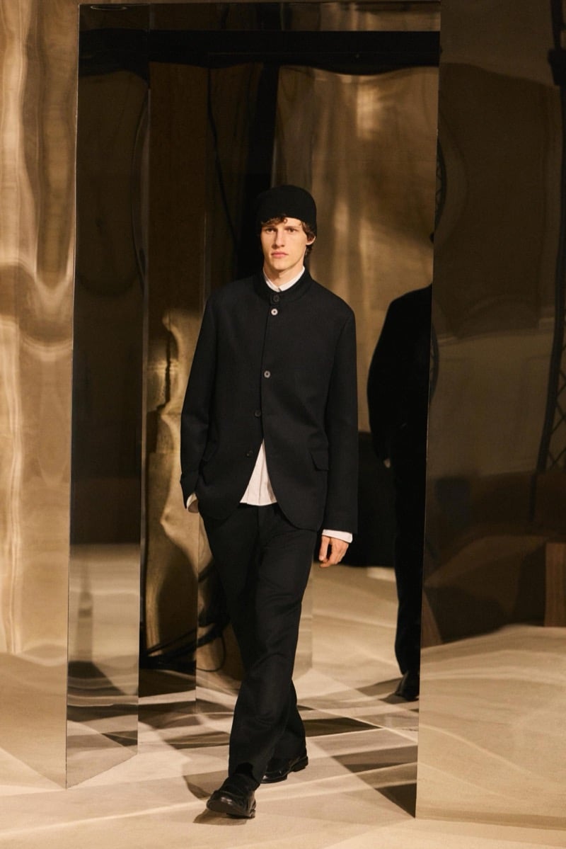 Massimo Dutti Limited Edition fall-winter 2026: Model wears a black buttoned jacket and trousers with a white shirt and black knit cap.