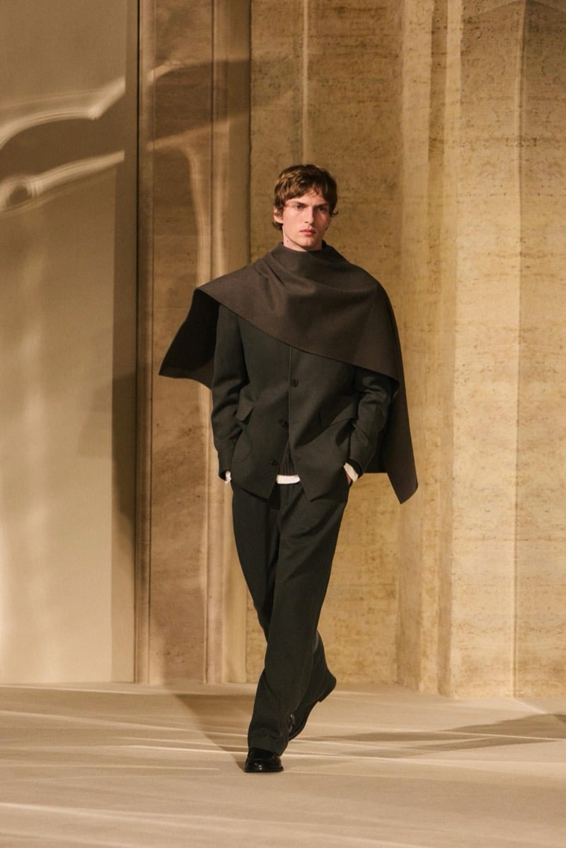Massimo Dutti Limited Edition fall-winter 2026: Model walks in an olive jacket and trousers with a broad brown scarf draped over his shoulders.
