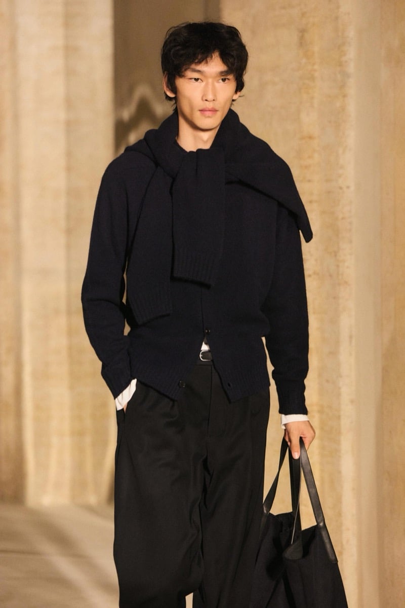 Massimo Dutti Limited Edition fall-winter 2026: Model wears a dark sweater and scarf with pleated trousers, carrying a black tote.