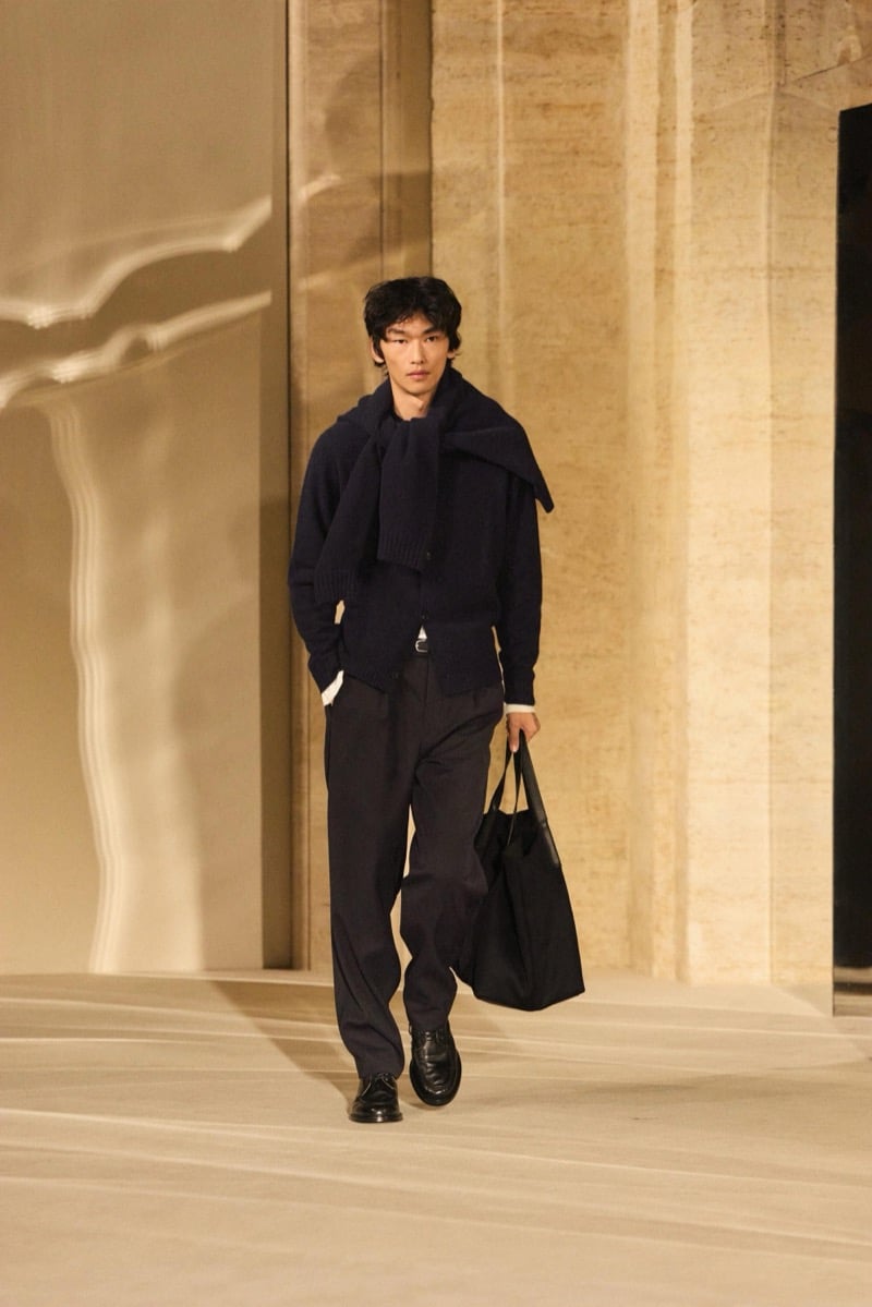 Massimo Dutti Limited Edition fall-winter 2026: Model walks in a dark knit and draped scarf with wide trousers and a black tote.