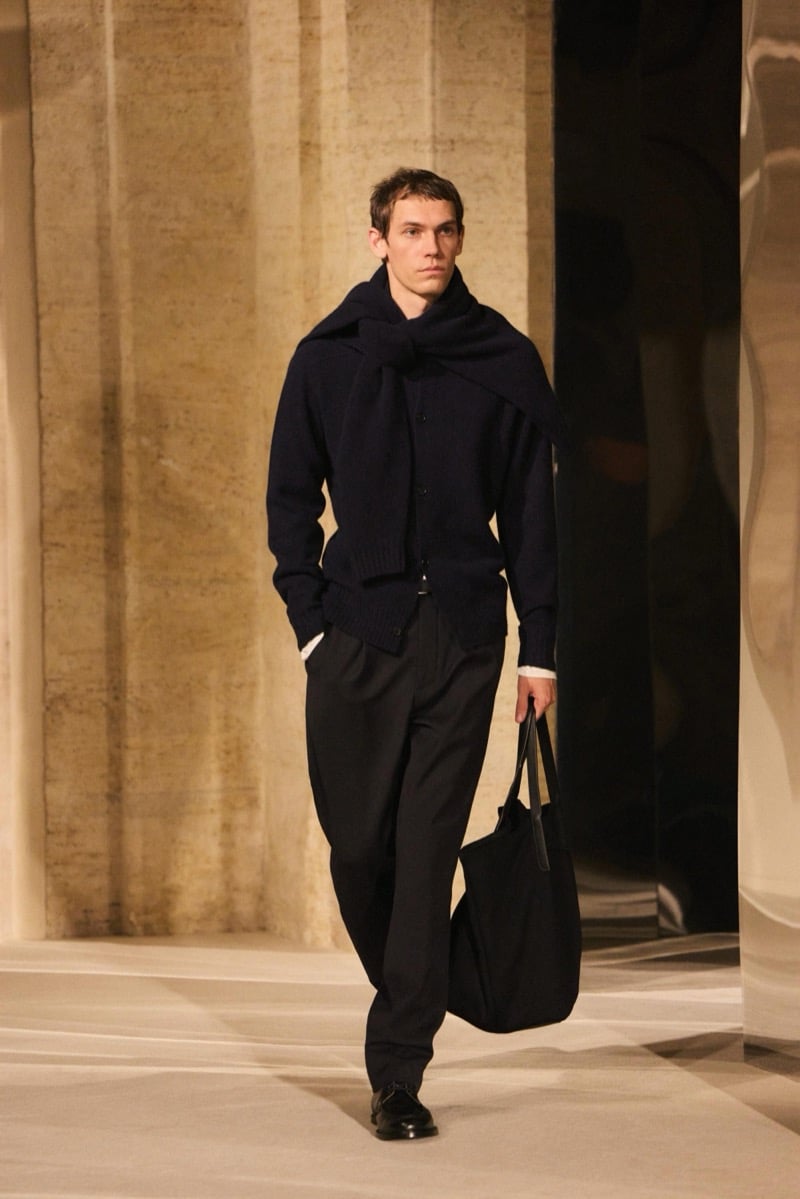 Massimo Dutti Limited Edition fall-winter 2026: Model wears a dark sweater, wrapped scarf, and wide pleated trousers, carrying a tote.