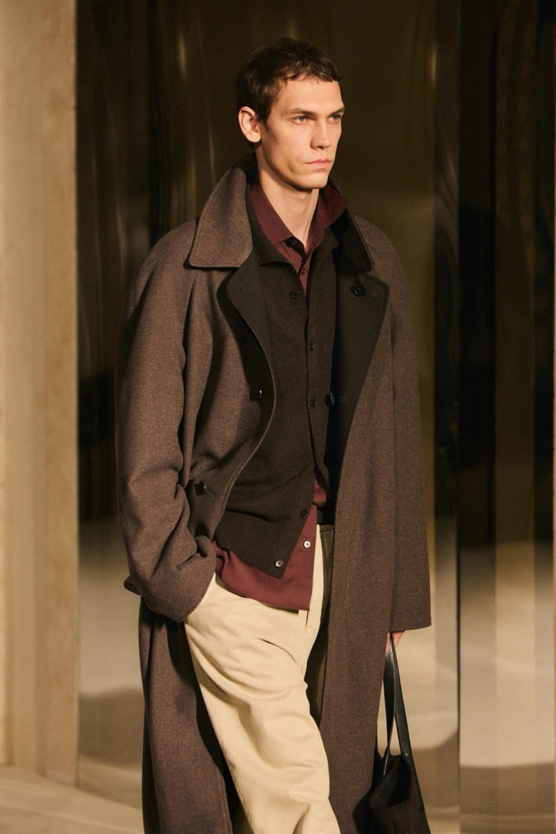 Massimo Dutti Limited Edition fall-winter 2026: Model wears a brown overcoat over a dark cardigan and burgundy shirt with beige trousers.
