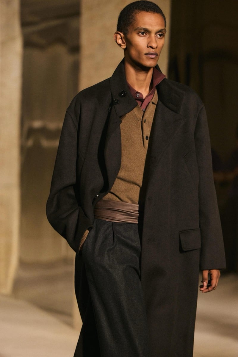 Massimo Dutti Limited Edition fall-winter 2026: Model wears a dark jacket over a tan knit and burgundy shirt with wide dark trousers.