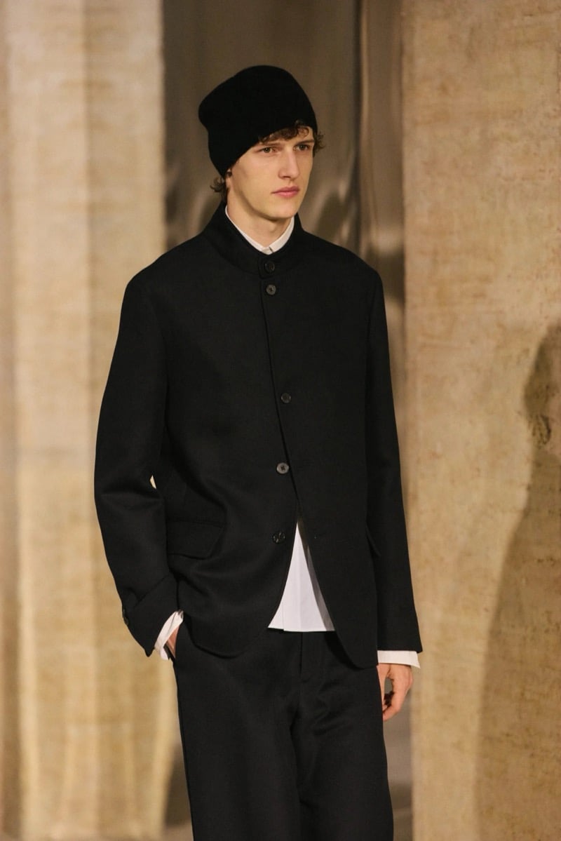 Massimo Dutti Limited Edition fall-winter 2026: Model wears a black knit cap and buttoned jacket over a white shirt with black trousers.