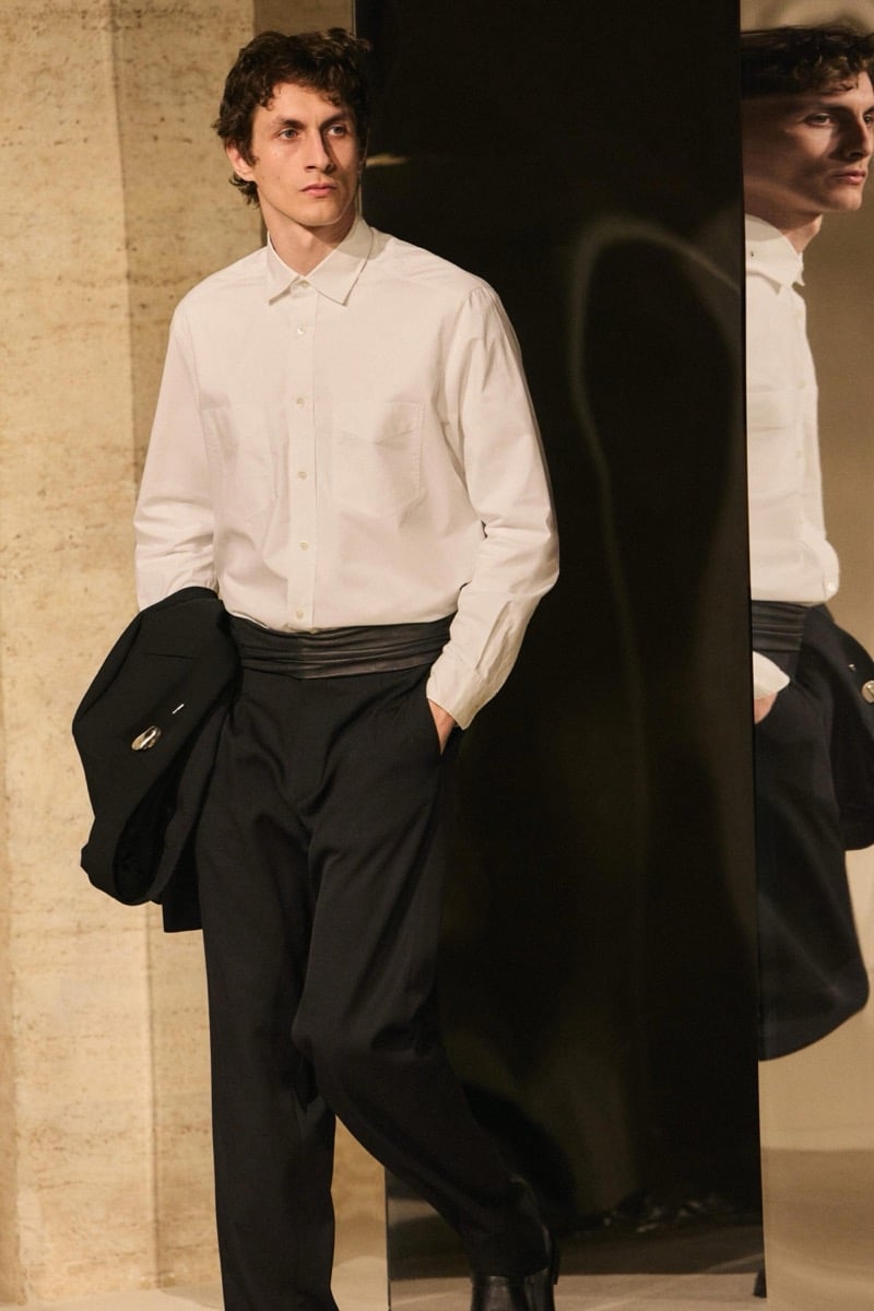 Massimo Dutti Limited Edition fall-winter 2026: Model wears a white button-up shirt with black pleated trousers, carrying a black jacket.