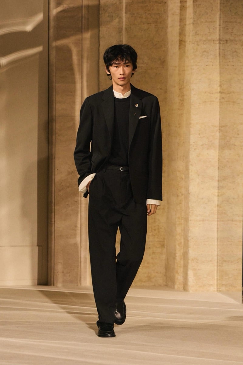 Massimo Dutti Limited Edition fall-winter 2026: Model walks in a black blazer and sweater over a white shirt with wide black trousers.