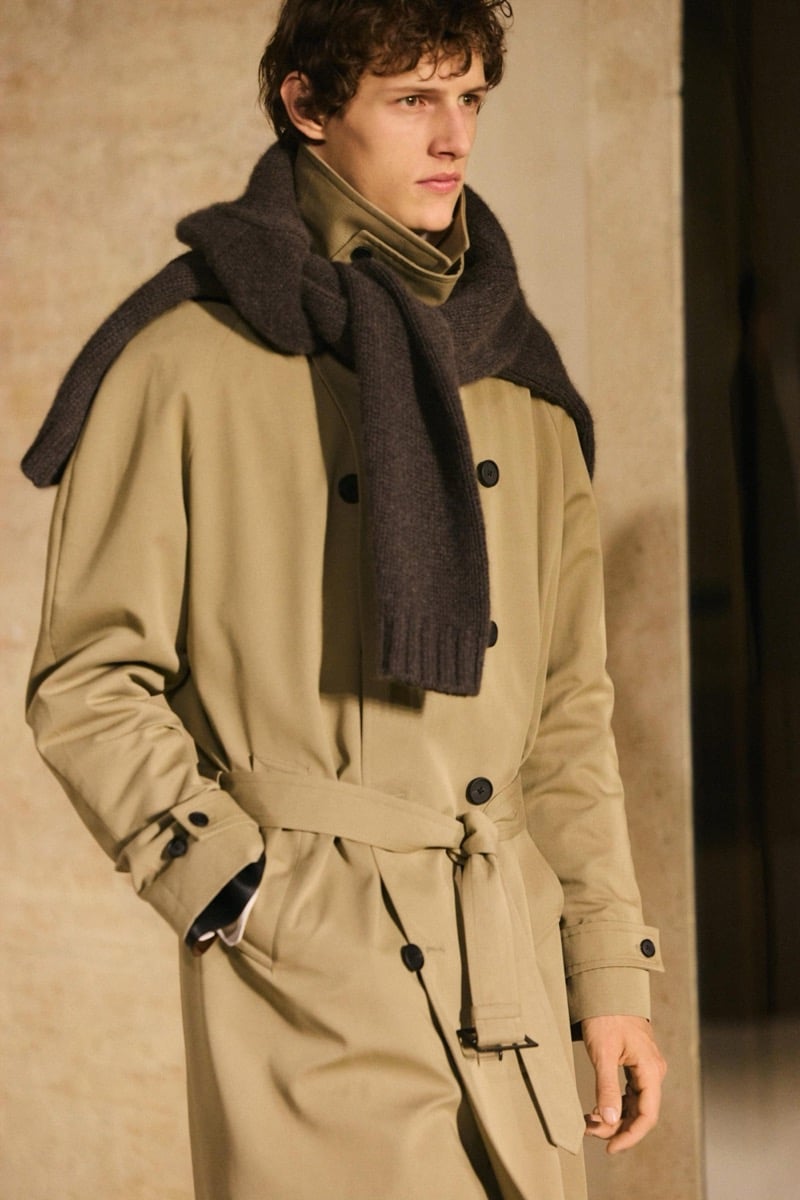 Massimo Dutti Limited Edition fall-winter 2026: Close-up of a model wearing a belted khaki trench coat with layered scarves.