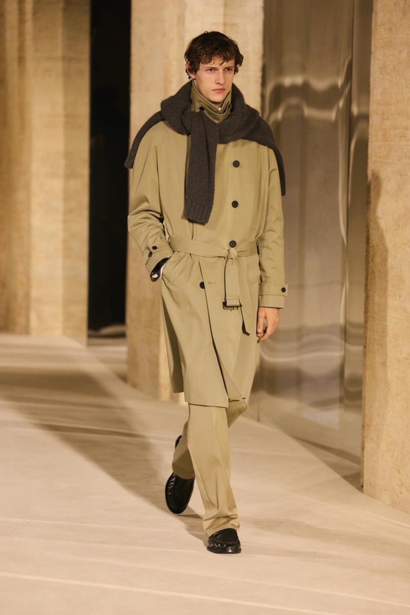 Massimo Dutti Limited Edition fall-winter 2026: Model walks in a belted khaki trench coat and matching trousers with a dark scarf.