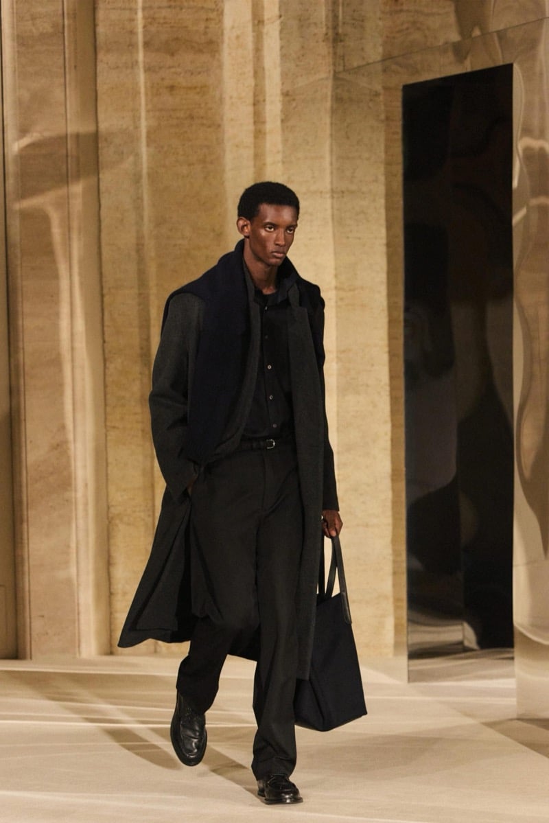 Massimo Dutti Limited Edition fall-winter 2026: Model wears a charcoal overcoat and dark layered separates, carrying a black tote.