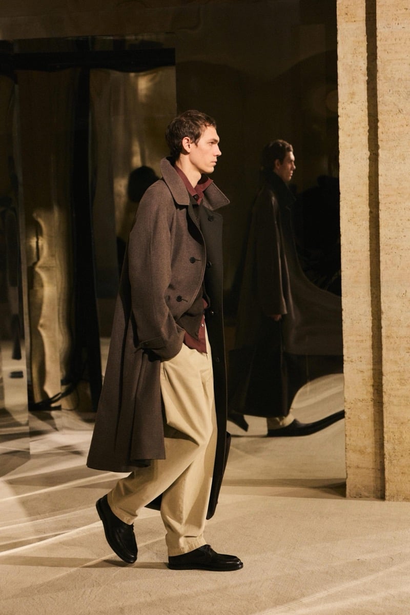 Massimo Dutti Limited Edition fall-winter 2026: Model walks in a brown overcoat, dark cardigan, and burgundy shirt with beige trousers.