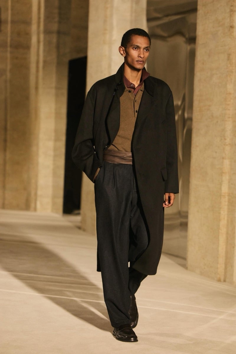 Massimo Dutti Limited Edition fall-winter 2026: Model wears a dark jacket over a tan knit and burgundy shirt with wide pleated trousers.