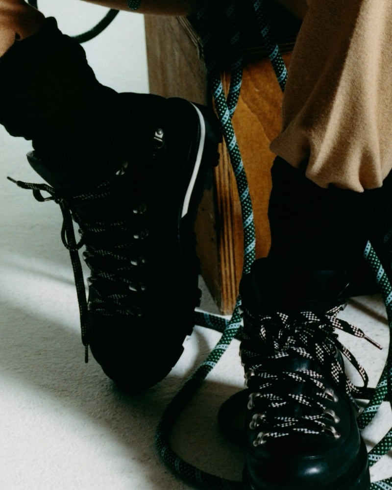 Close-up of black lace-up hiking boots with patterned laces beside a green and light blue climbing rope and a wooden crate