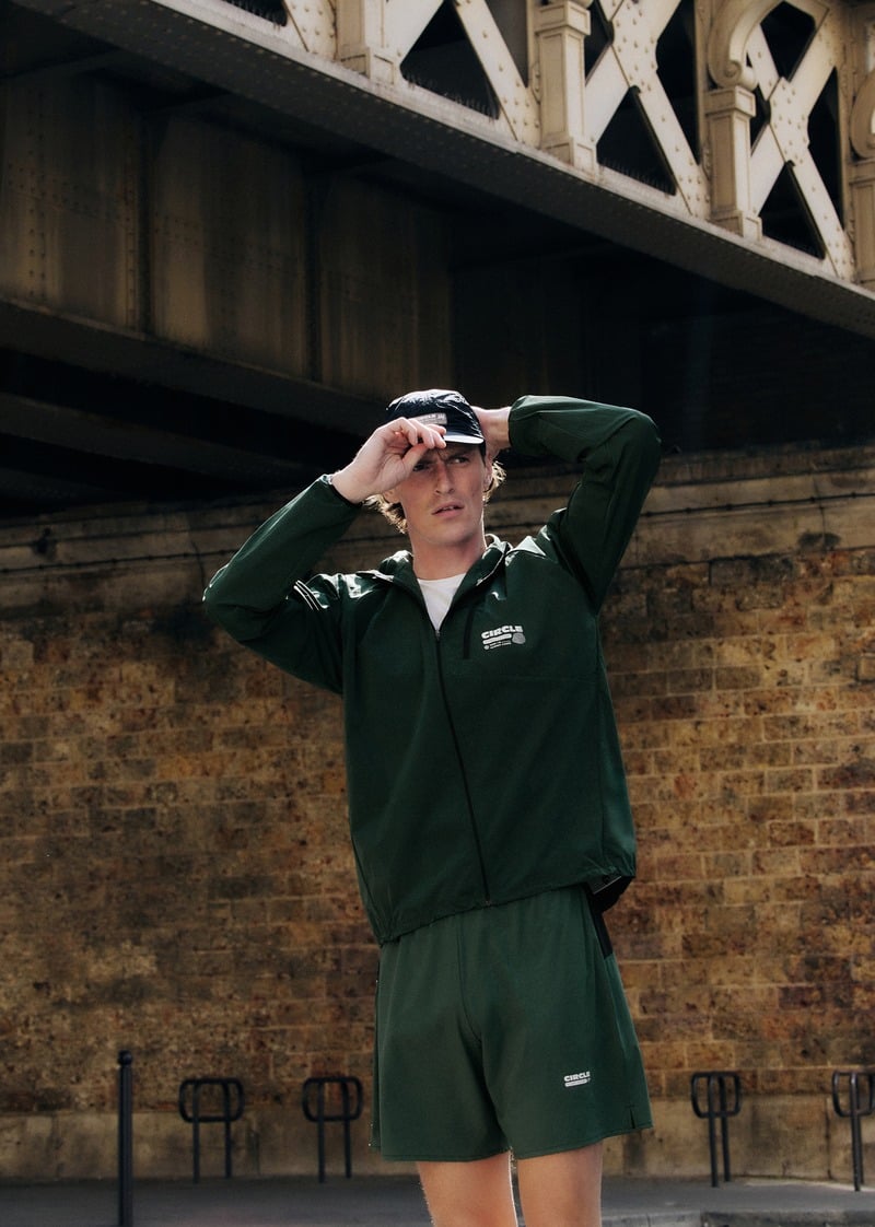 Myles Crosby adjusting a black cap while wearing a green zip-front running jacket