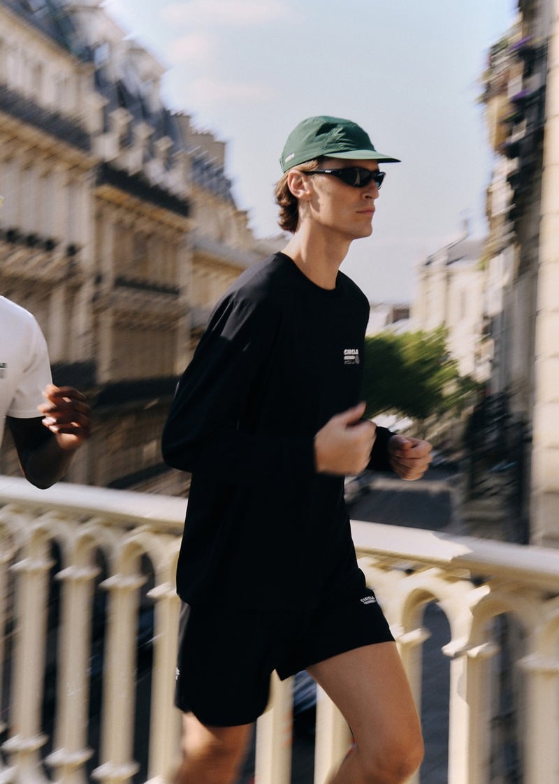 Myles Crosby running beside a stone balustrade in a black long-sleeve top and green cap
