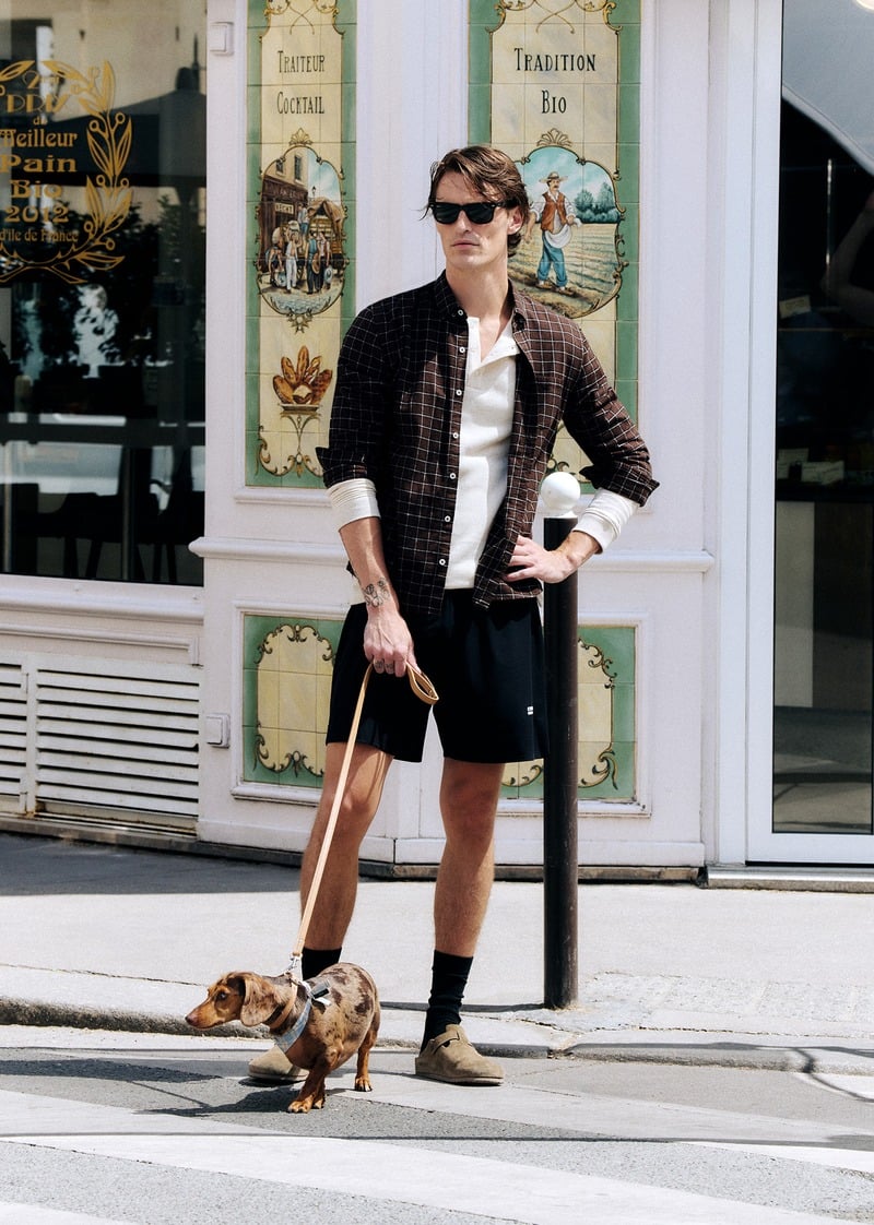 Myles Crosby walking a dog in black shorts, an open checked shirt and sunglasses