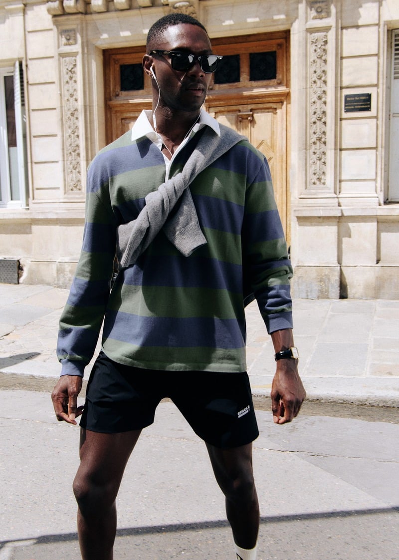 Sadiq Desh wearing black running shorts with a striped rugby shirt and a sweater across his chest