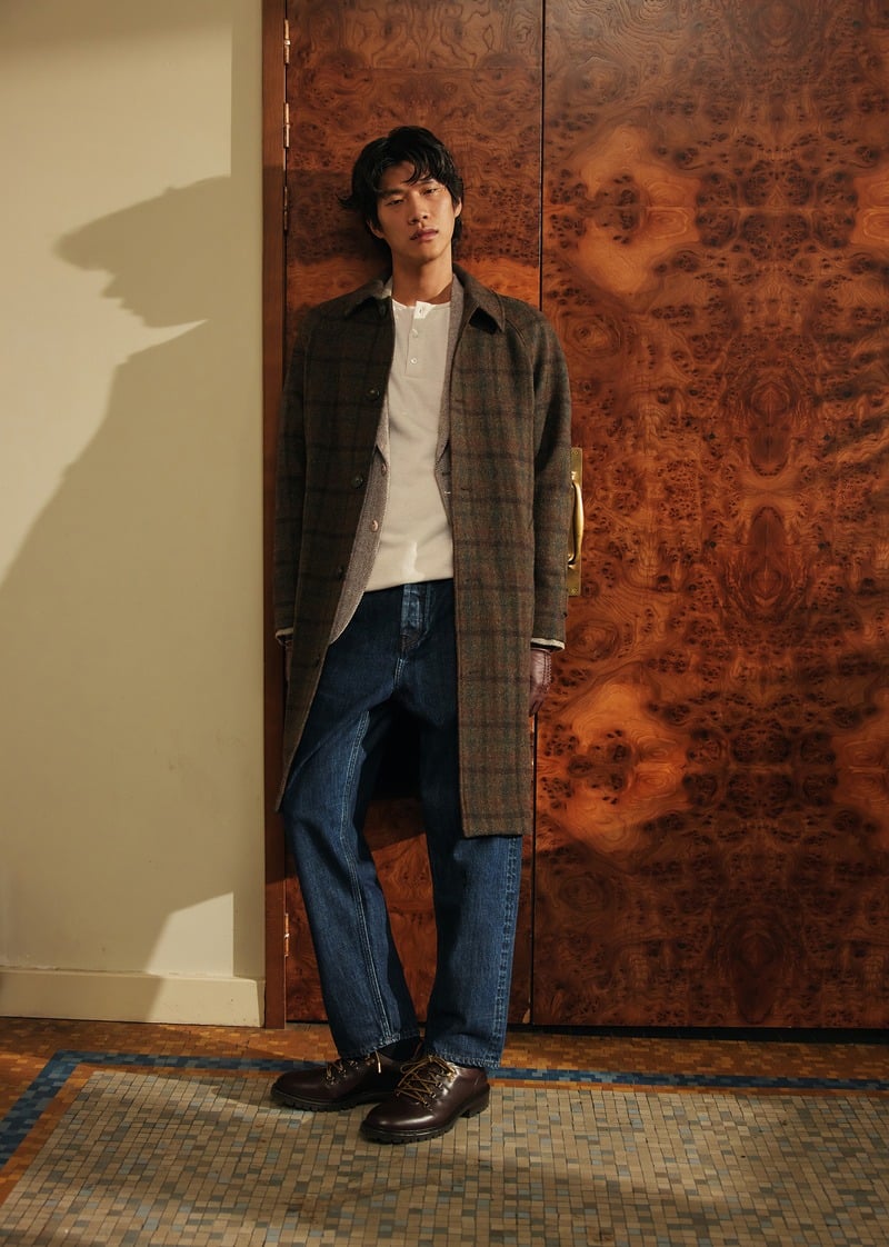 Sanggun Lee stands in a long checked Mikkelsen coat over a white shirt and blue jeans.