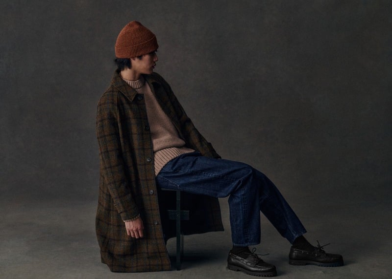 Sanggun Lee sits in a checked Mikkelsen coat, rust beanie, taupe sweater and blue jeans.