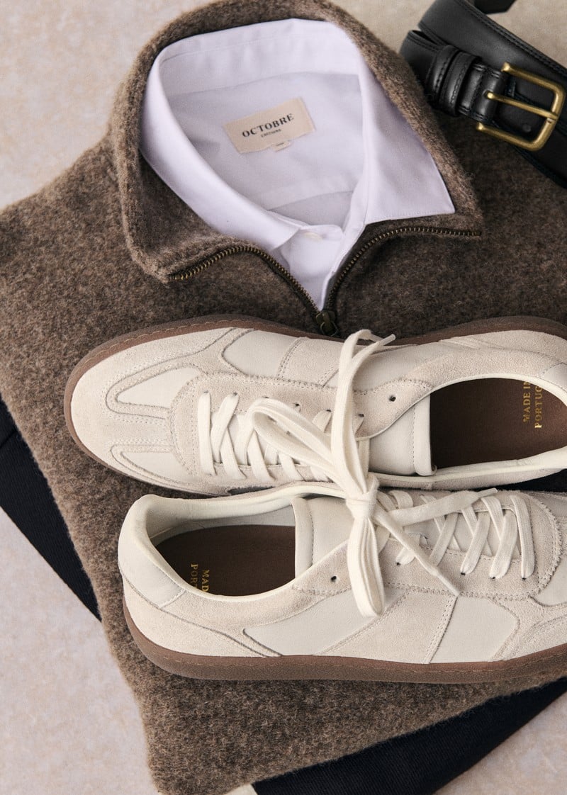 White Halrin sneakers rest on a knit sweater and white shirt.
