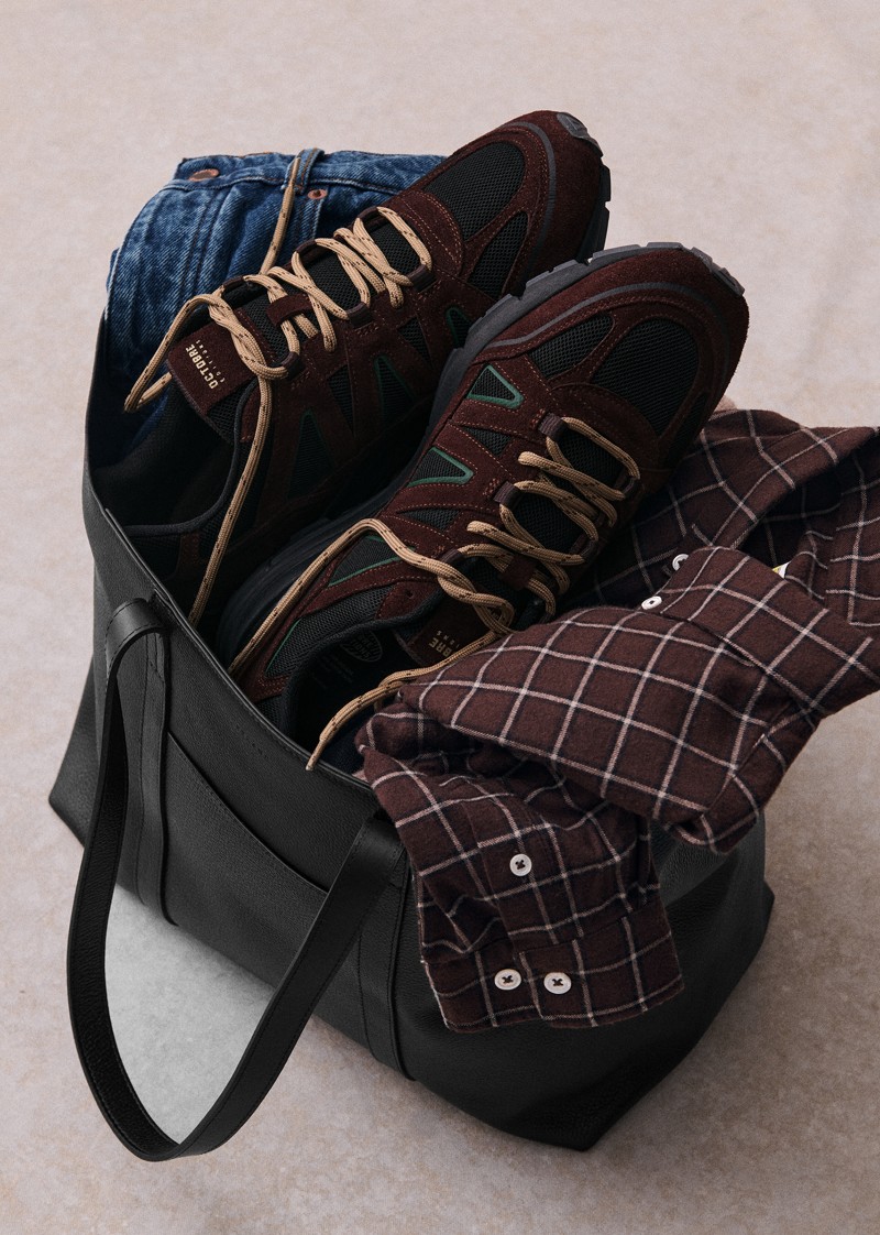 Brown and black OE10 sneakers sit beside folded clothing and a bag.