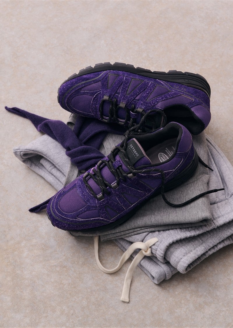 Purple OE10 sneakers rest on folded gray clothing.