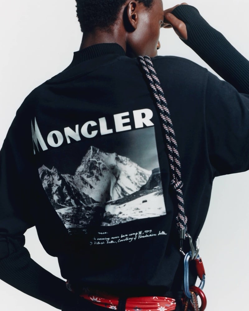 Olu Charles seen from behind in a black Moncler sweatshirt with a mountain photograph printed on the back, a rope and carabiners over his shoulder