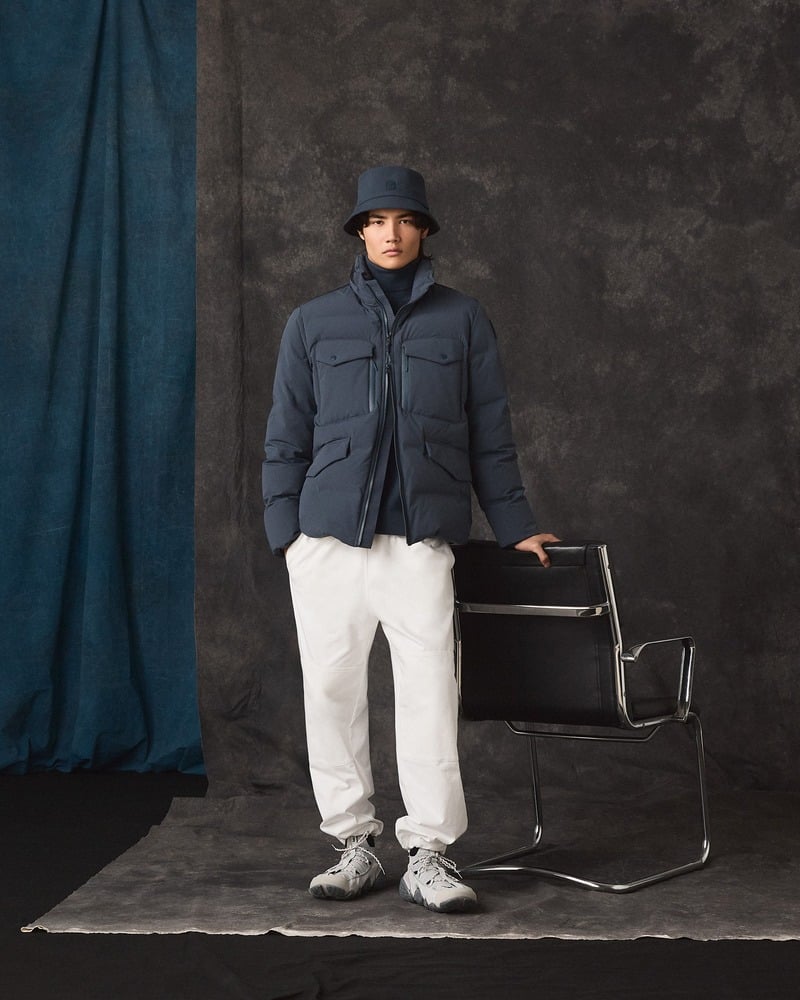 Model wears a navy Parajumpers jacket with white trousers, sneakers, and a dark bucket hat.