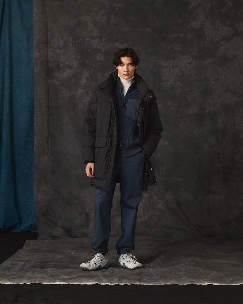 Model wears a dark Parajumpers coat over coordinated layers with gray sneakers.