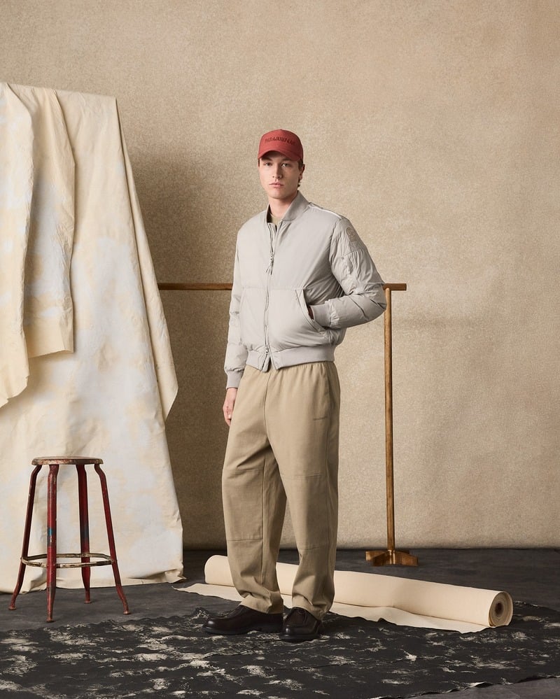Model wears a gray Parajumpers jacket with loose beige trousers and a red cap.