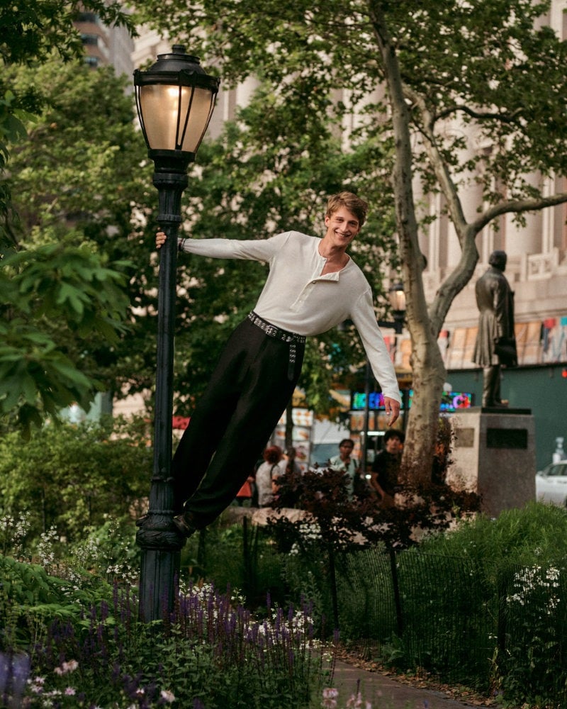 Vasko Luyckx swings from a lamppost in an ecru Henley and wide dark trousers.