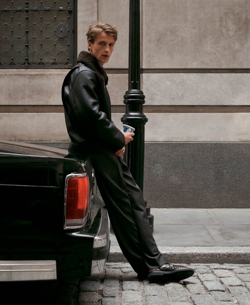 Vasko Luyckx stands beside a parked car in a black leather jacket and dark trousers.