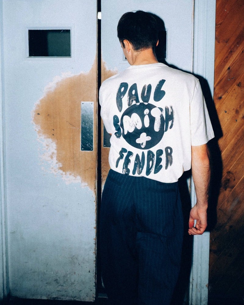 A member of Legss wears a white Paul Smith + Fender graphic T-shirt viewed from behind.