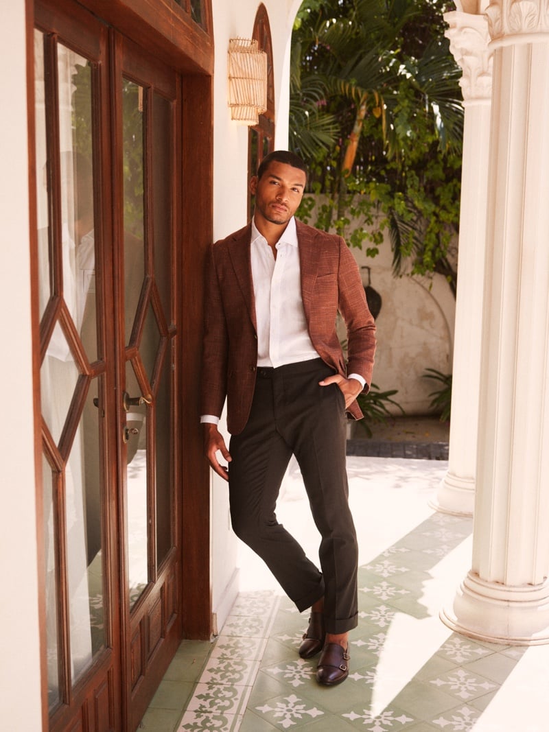Paulo Lopes Lucio wears a rust blazer, white open-collar shirt and dark trousers beside a courtyard doorway.