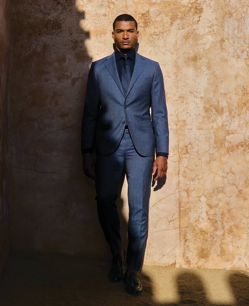 Paulo Lopes Lucio wears a blue suit with a dark shirt and tonal tie against an ochre wall.