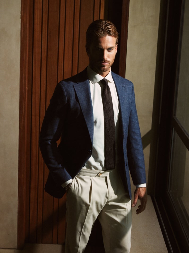 Gonçalo Campos wears a navy blazer, white shirt, dark tie and light trousers beside a wooden doorway.
