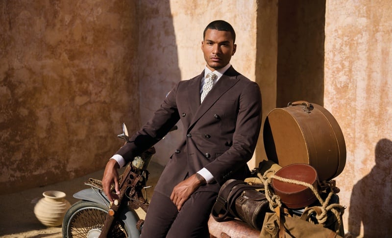 Paulo Lopes Lucio sits on a luggage-laden motorcycle wearing a dark double-breasted suit and patterned tie.