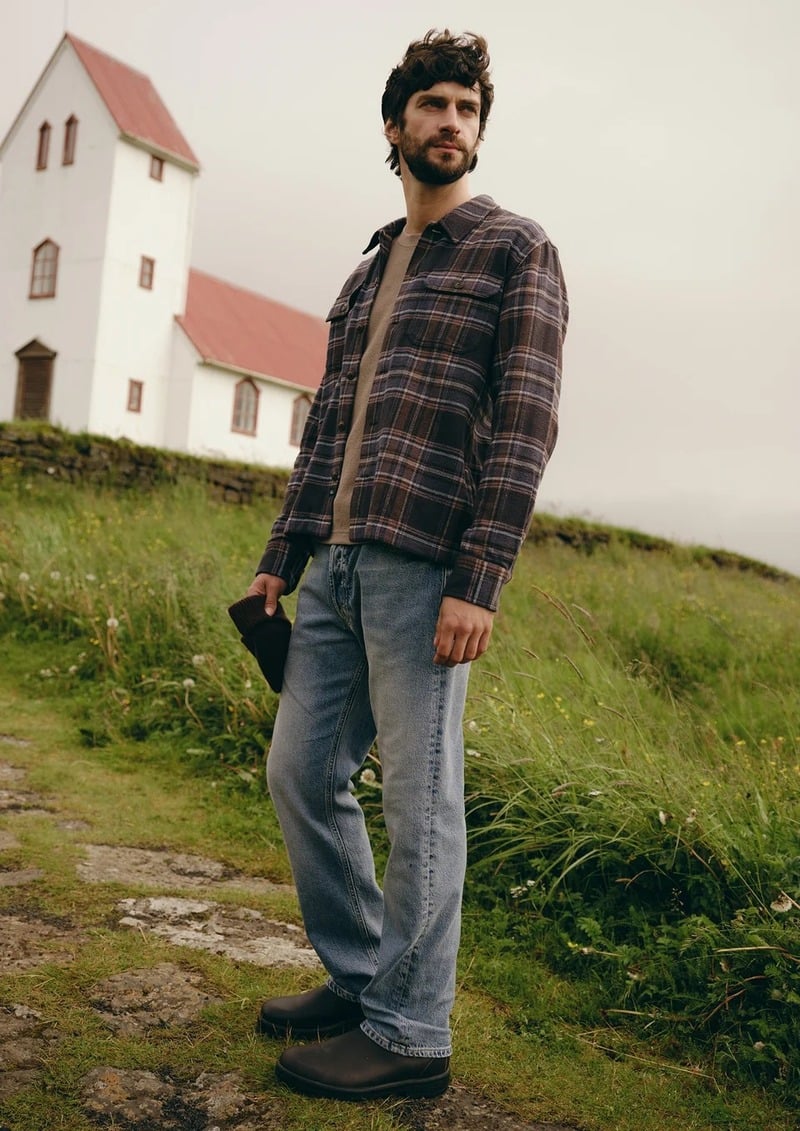 Matthew Bell stands beside a painted house in a plaid overshirt and faded jeans.